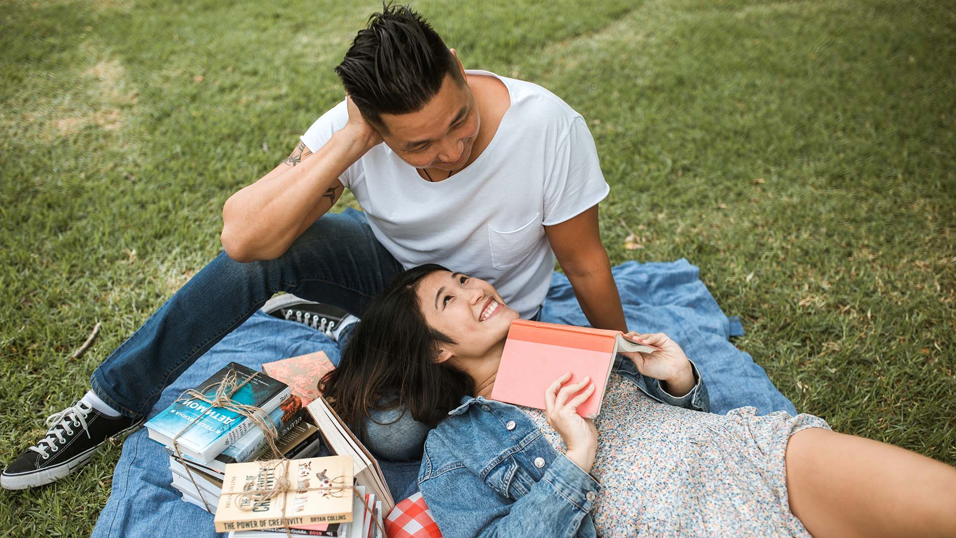 Two people relaxing on picnic blanket reading books in the sun.